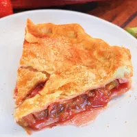 Angled view of a slice of pie with a buttery double crust filled with a strawberry rhubarb filling - Hostess At Heart