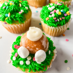 Cupcakes decorated with a grass tip with a bunny butt made from a donut hole sticking out.