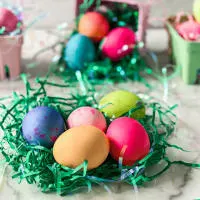 Tableview photo of dyed Easter Eggs sitting on shredded of green grass with cartons of colored eggs sitting in the background