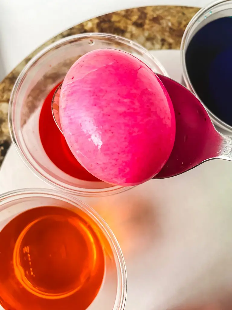 A freshly dipped pink dyed Easter egg sitting on a spoon