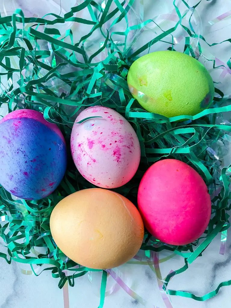 Dyed eggs sitting in shredded green grass.