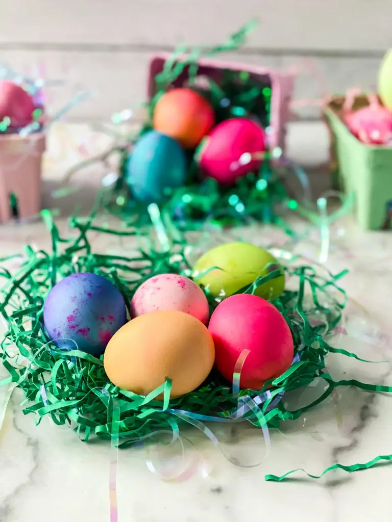 Multi-colored hard boiled eggs sitting in shredded green paper.