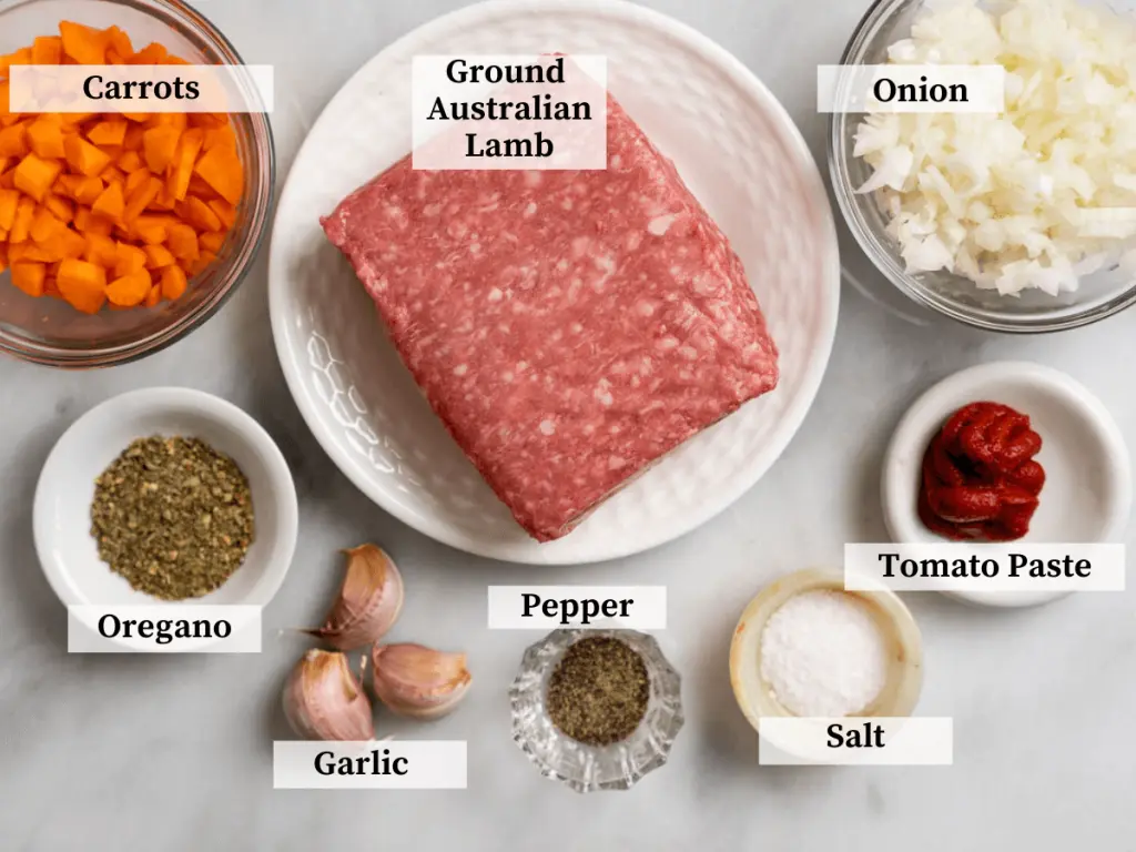Top down photo of meat sauce ingredients including ground lamb, onion, carrots, tomato paste, garlic, Italian seasoning, salt, and pepper.