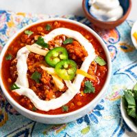 Close-up top down photo of a bowl of lentil chili garnished with sour cream, sliced jalapenos, cilantro and cheese.