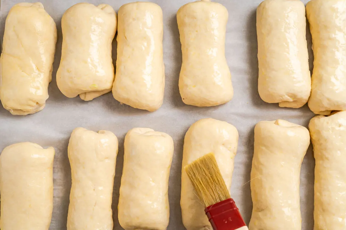 Egg wash being applied to risen shaped and filled dough.