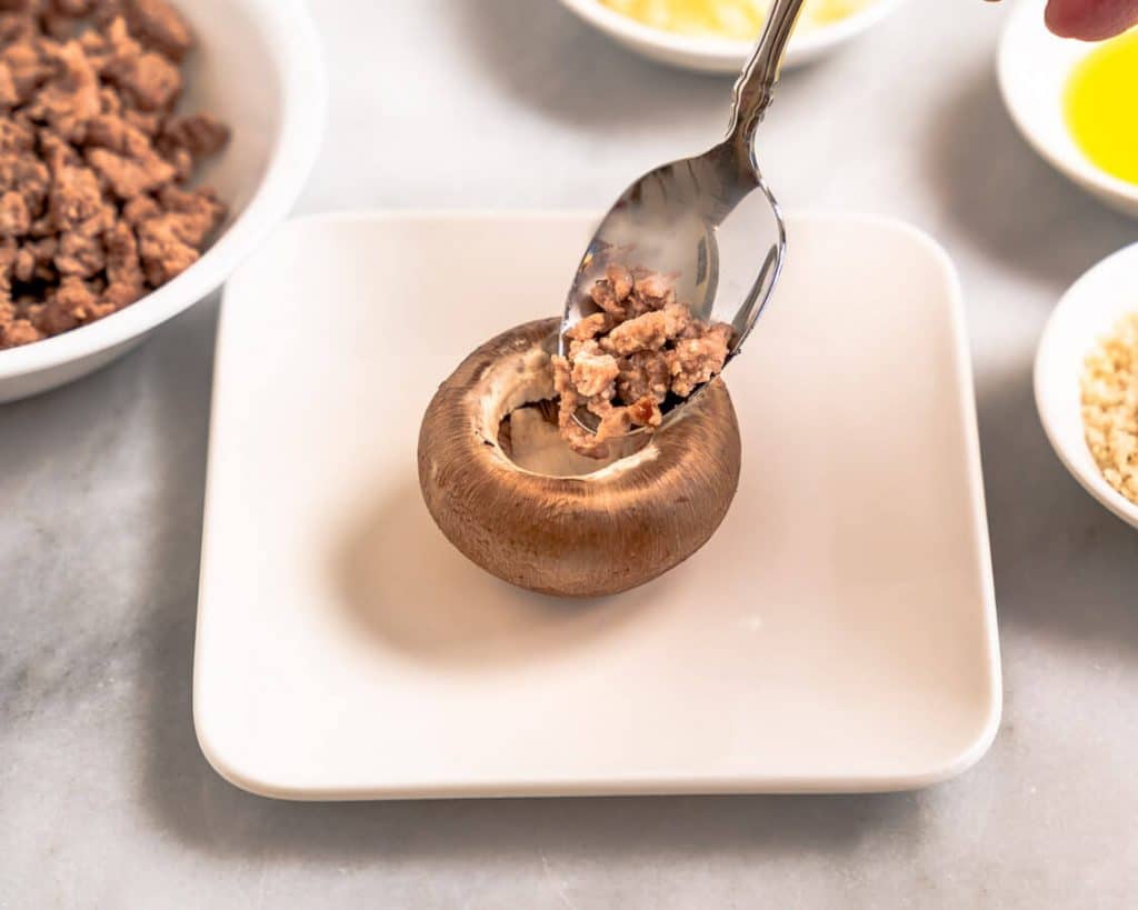 Meat filling being spooned into a mushroom cap.