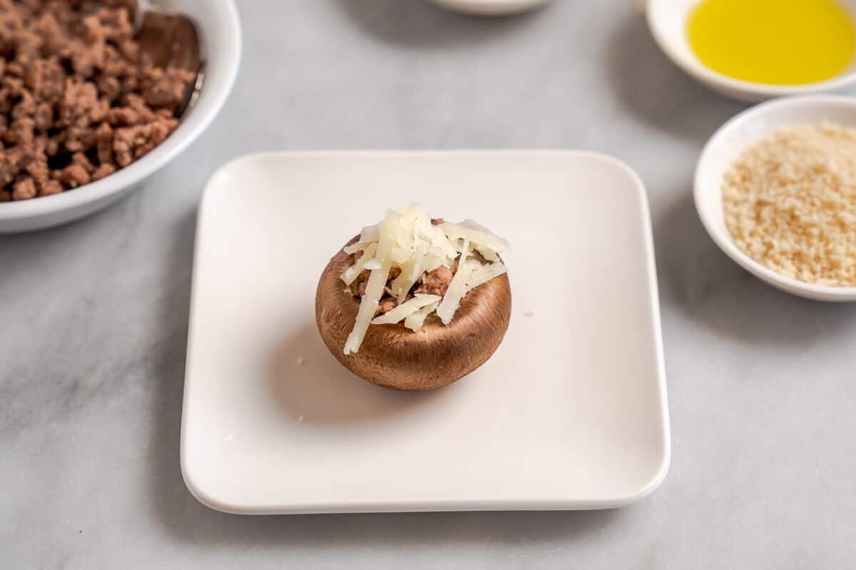 A stuffed mushroom topped with shredded cheese and bread crumbs ready to be broiled.