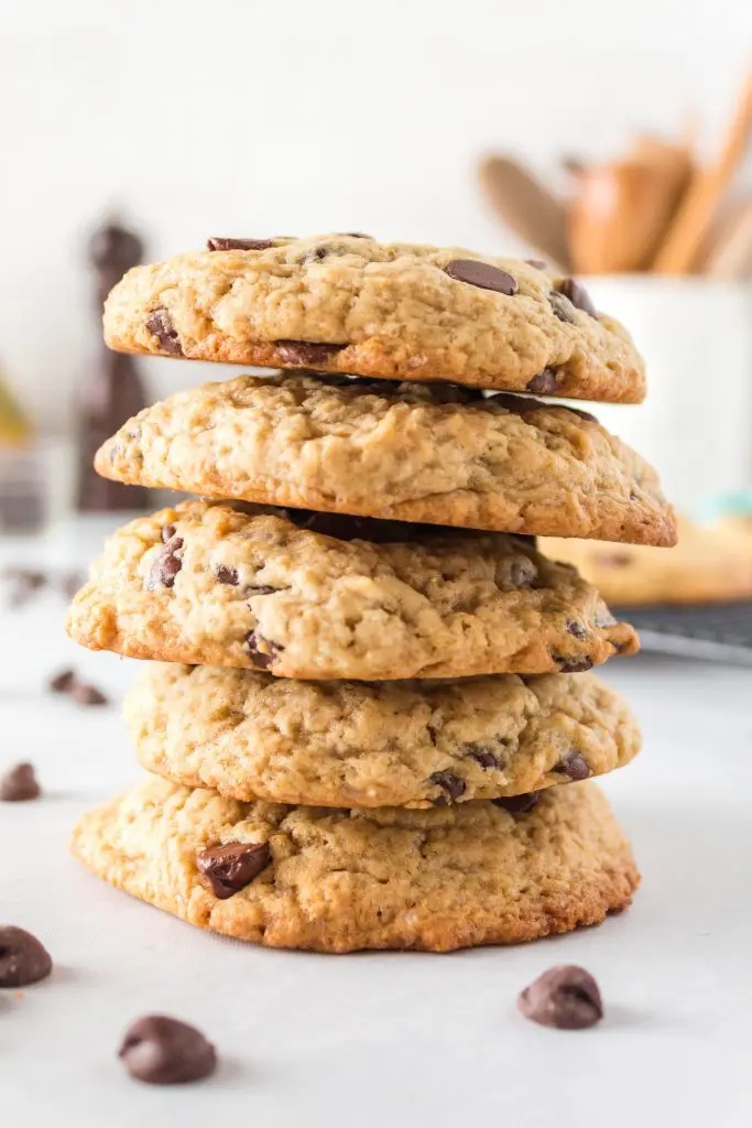 A stack of chocolate chip cookies with chips scattered around the bottom.