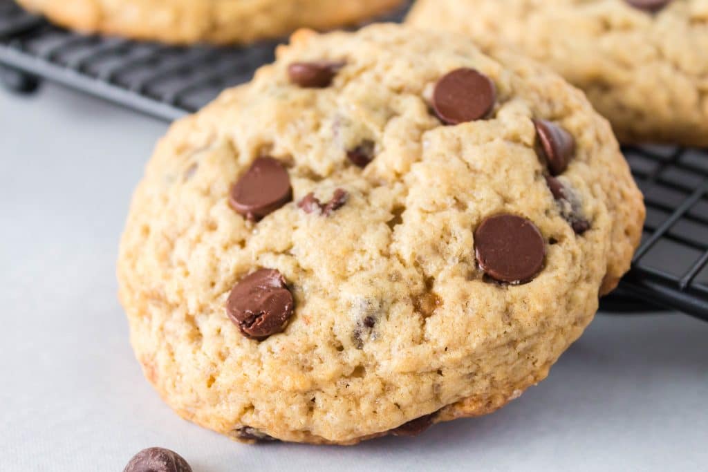 Side view of a cookie filled with chocolate chips resting against a cooking rack.