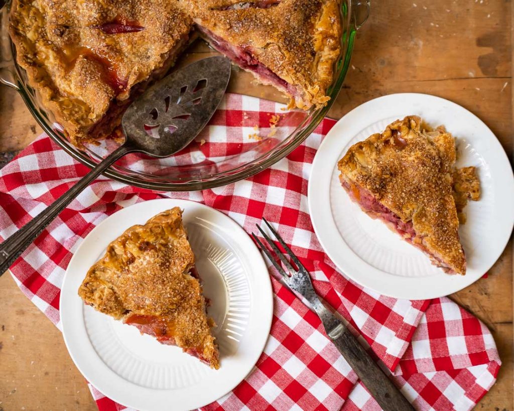 Flay lay photo of two slices of pie on a red checkered napkin with the cut pie in the background.