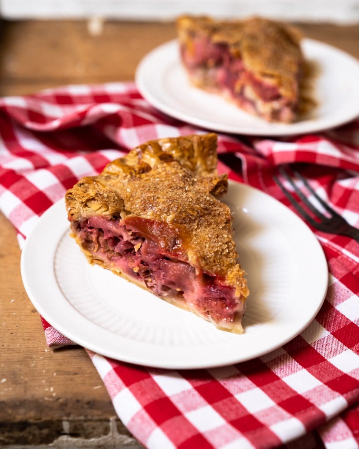 Single slice of strawberry rhubarb pie on a plate with other pieces in the background. 