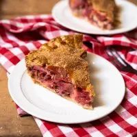 A single slice of a strawberry rhubarb pie recipe on a plate with a second slice in the background.