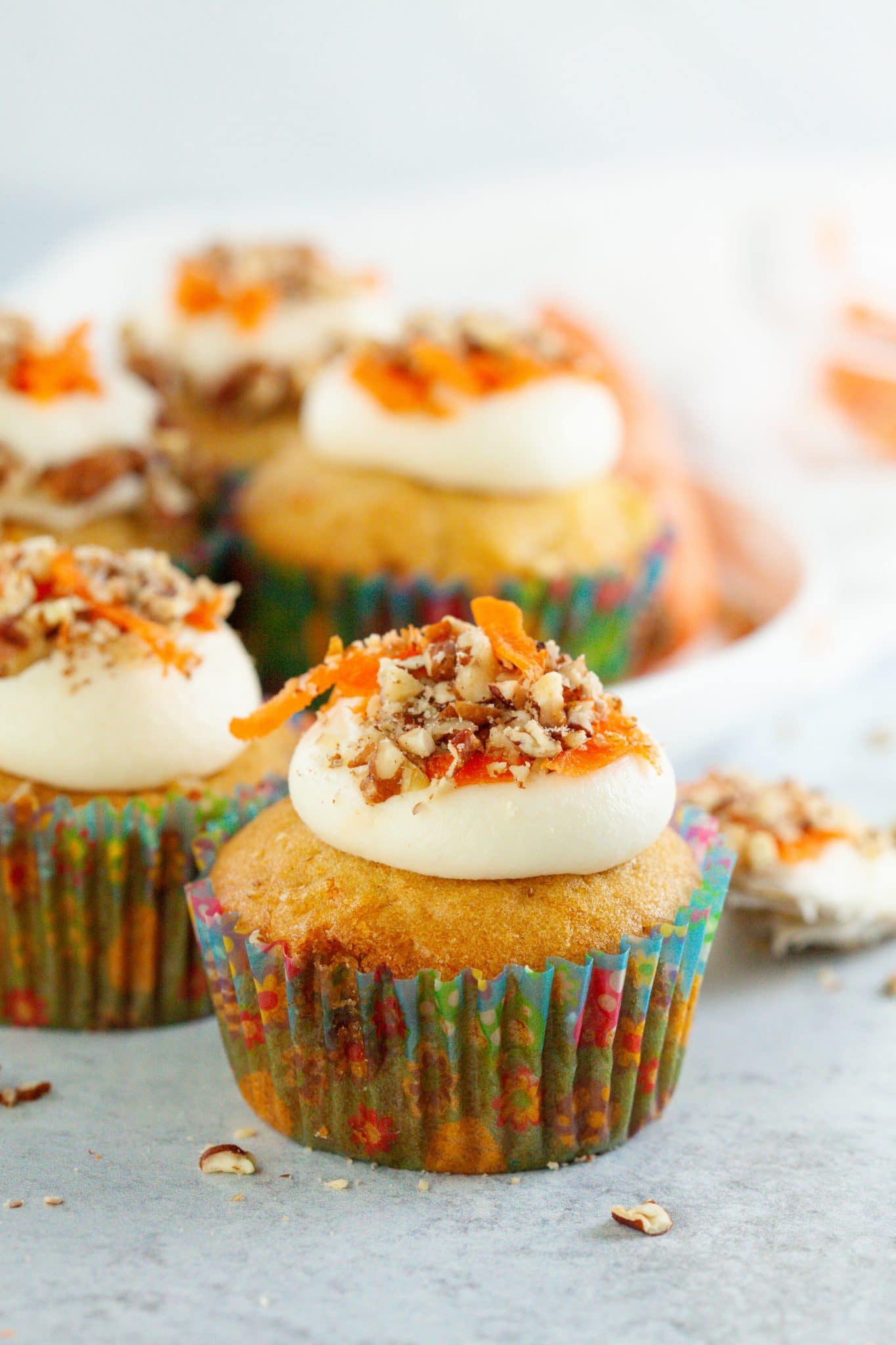 Carrot cupcakes beautifully decorated with cream cheese frosting, shredded carrots, and chopped pecans.