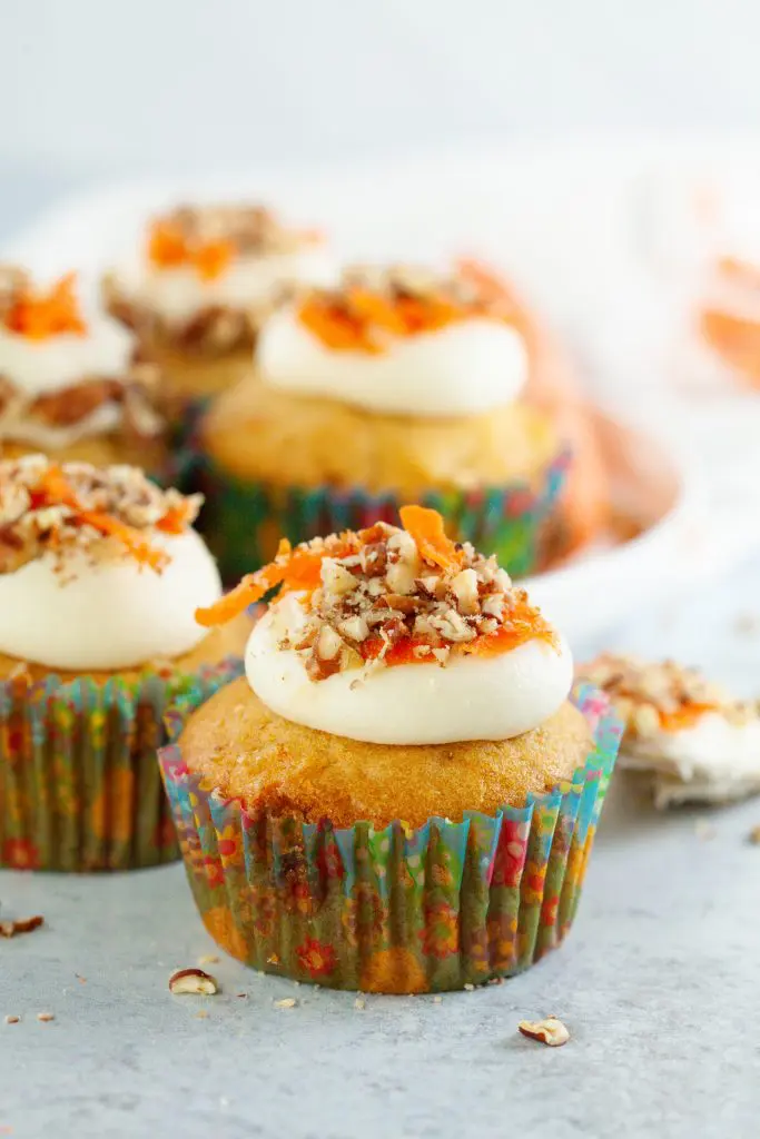 Carrot cupcakes beautifully decorated with cream cheese frosting, shredded carrots, and chopped pecans. 