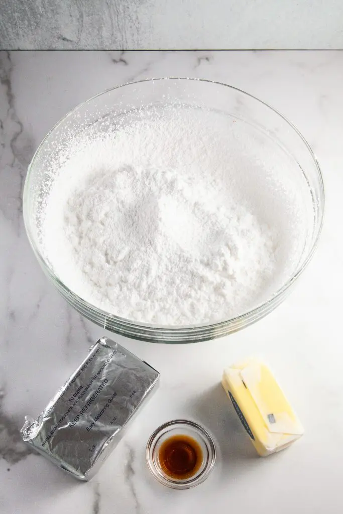 Ingredients for cream cheese frosting: powdered sugar in a bowl, cream cheese, butter, and vanilla.