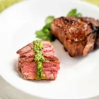 Sliced lamb with a drizzle of pesto in front of an uncut lamb chop