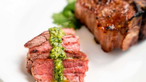 Sliced lamb with a drizzle of pesto in front of an uncut lamb chop