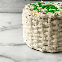 Close-up side view of a decorated Cake with a basket weave design and colorful flowers.