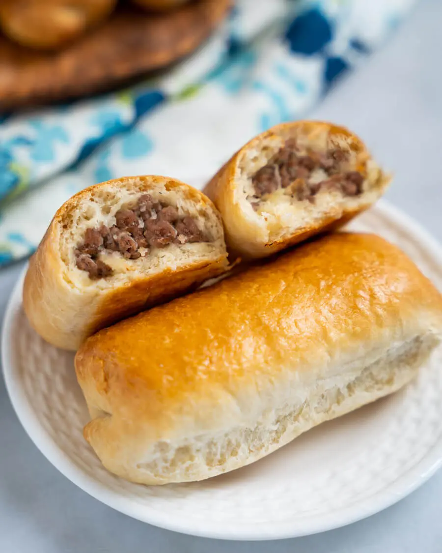 A meat bun cut in half showing cooked meat filling. The halves are leaning against a whole meat bun