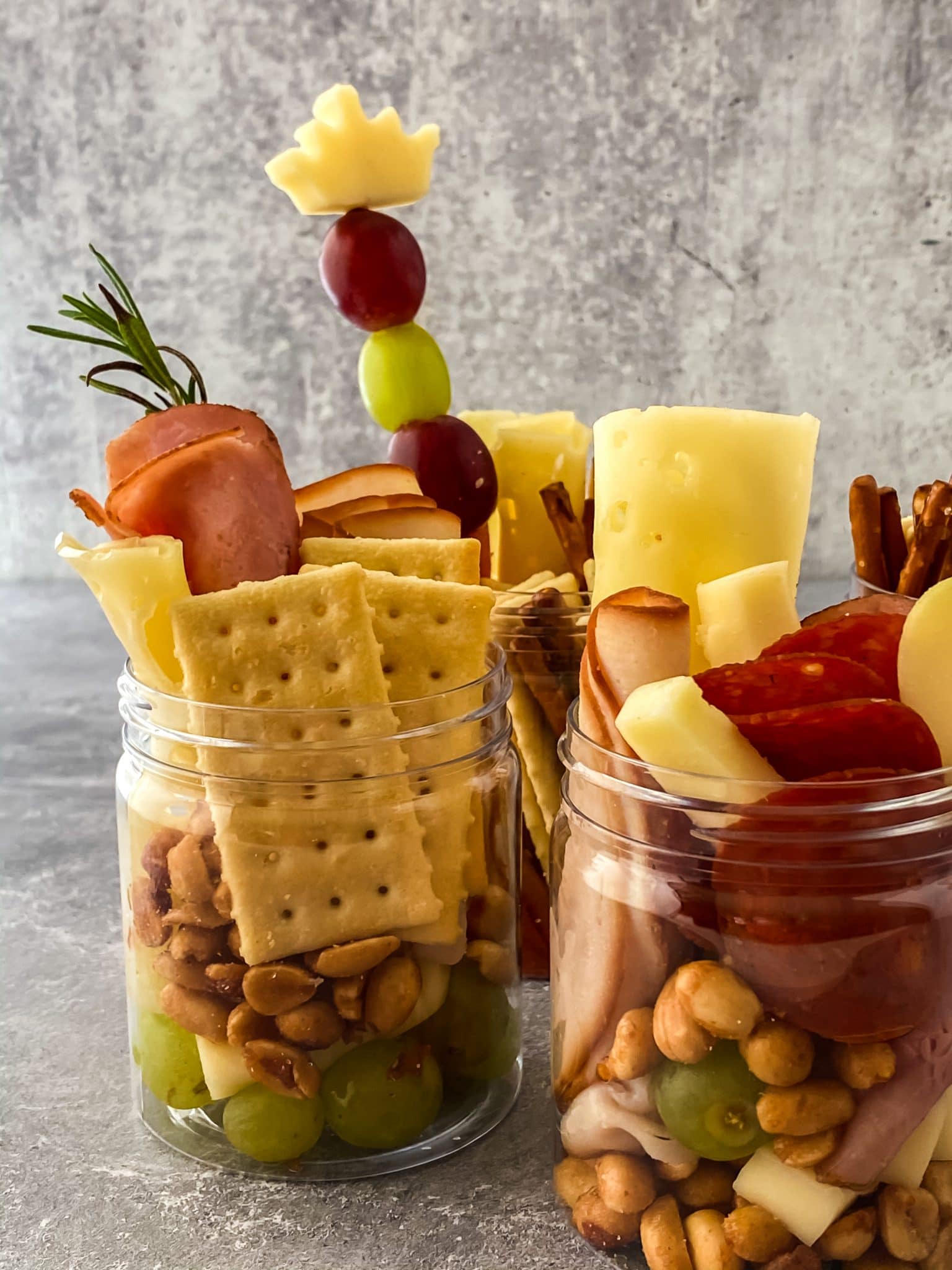 close up of small jars filled with meats, cheeses, crackers, nuts, and grapes