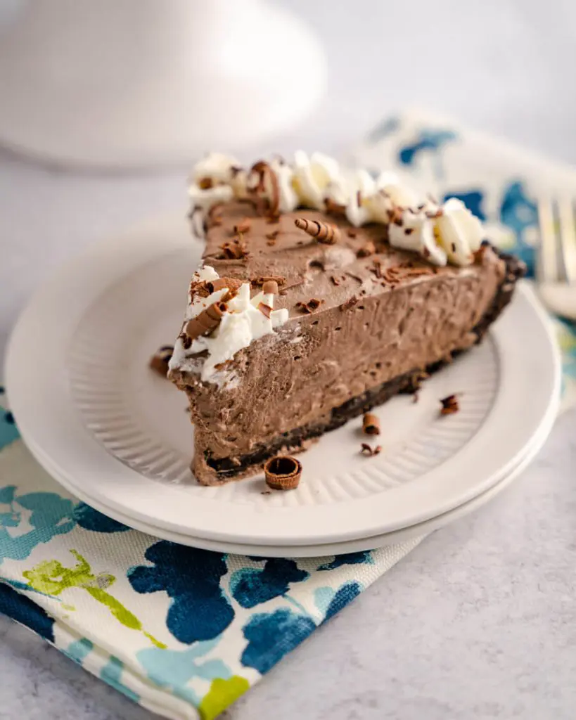 Side angle of a slice of chocolate cheesecake pie sitting on a plate over a multicolored napkin