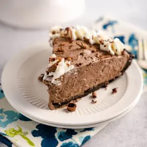 Side angle of a slice of chocolate cheesecake pie sitting on a plate over a multicolored napkin