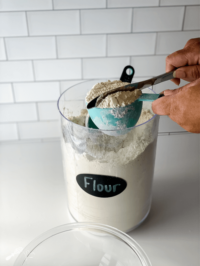 A butter knife is tapped over a measuring cup filled with flour to remove the air bubbles.