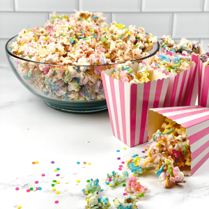 Striped popcorn boxes filled with multi-colored popcorn. The bowl of the popcorn sits in the background.