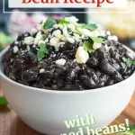 Side view of a bowl of black beans garnished with cilantro and a wedge of lime.