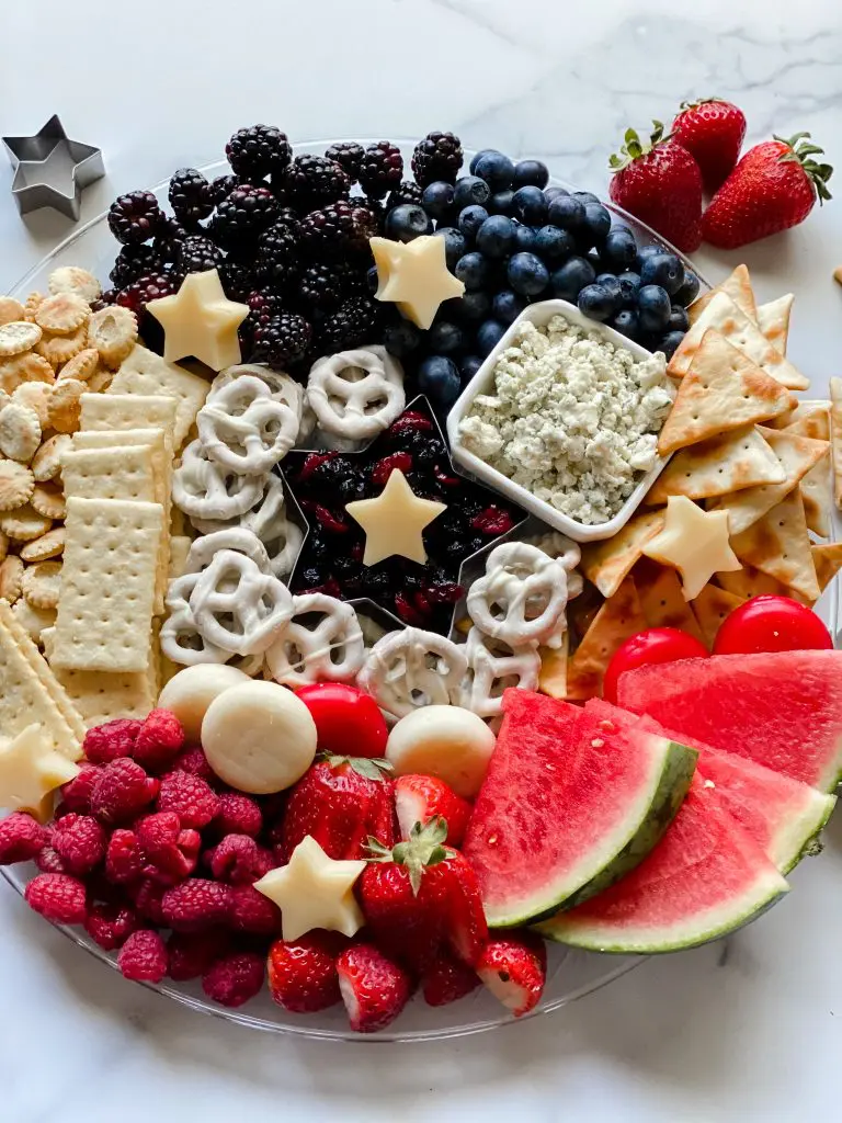 beautiful patriotic charcuterie board with crackers, cheese, and fruit on a tray with a granite surface underneath.