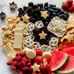 A tray filled with cheeses, fruits, pretzels, and crackers.