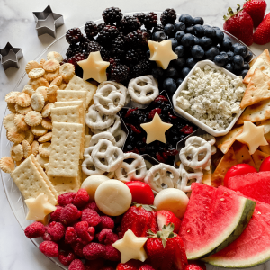 A tray filled with cheeses, fruits, pretzels, and crackers.
