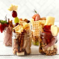Jars filled with sliced meats, cheeses, crackers, fruit, nuts and pretzels.