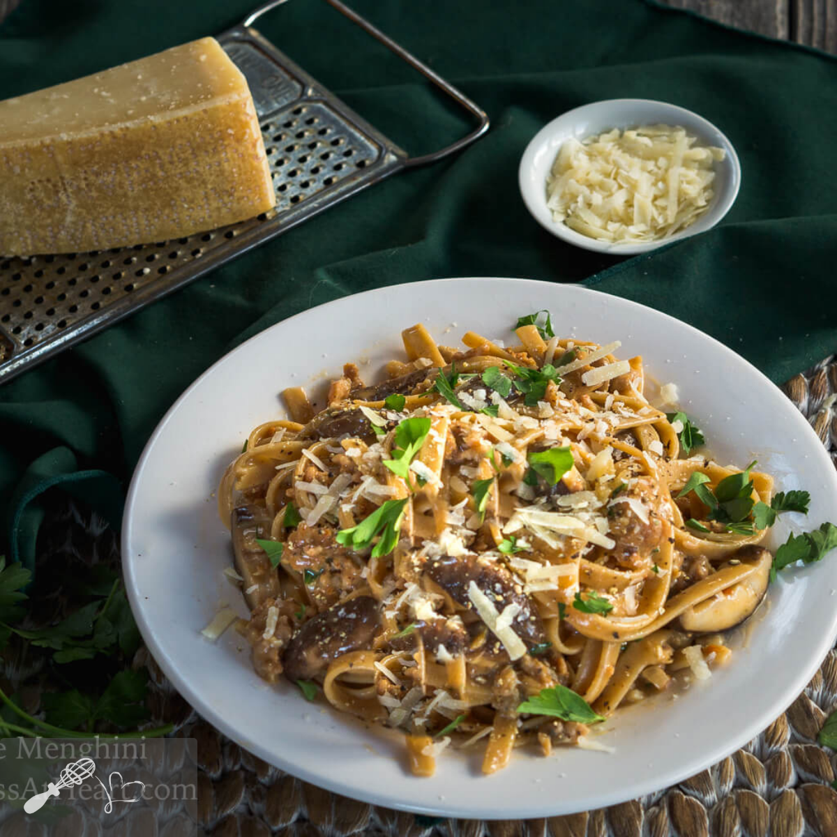 Top-down view of a plate holding Fettuccine Alfredo with Sausage garnished with parsley and cheese.