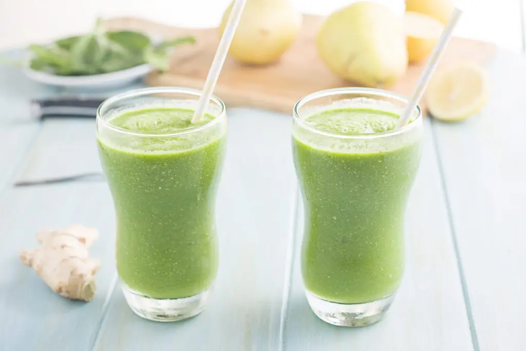Two glasses filled with green smoothies with straws.