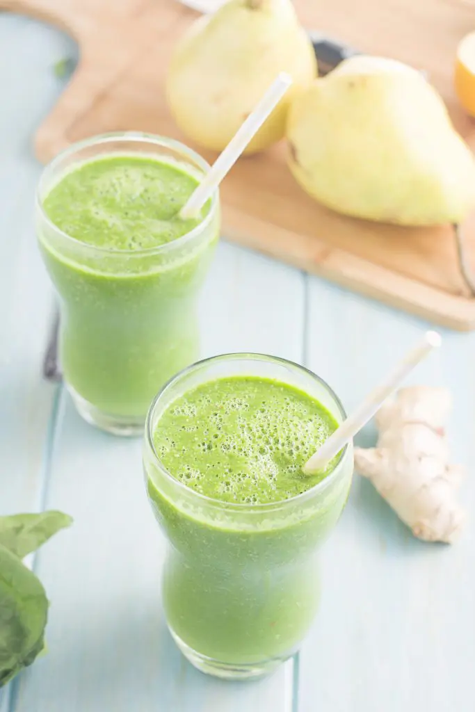 3/4 angle of two green smoothies with pears in the background.