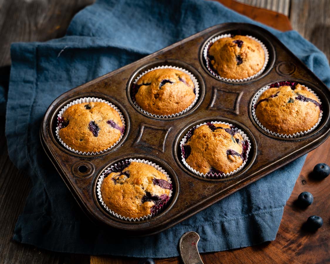 Top down view of a muffin tin filled with golden brown baked blueberry muffins