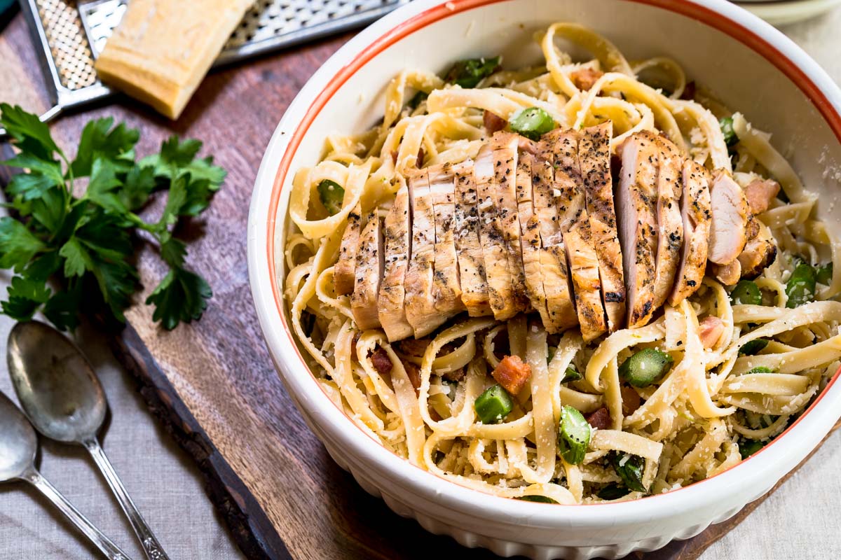 Top down photo of a bowl of fettuccine pasta topped with grilled chicken, asparagus and grated cheese.