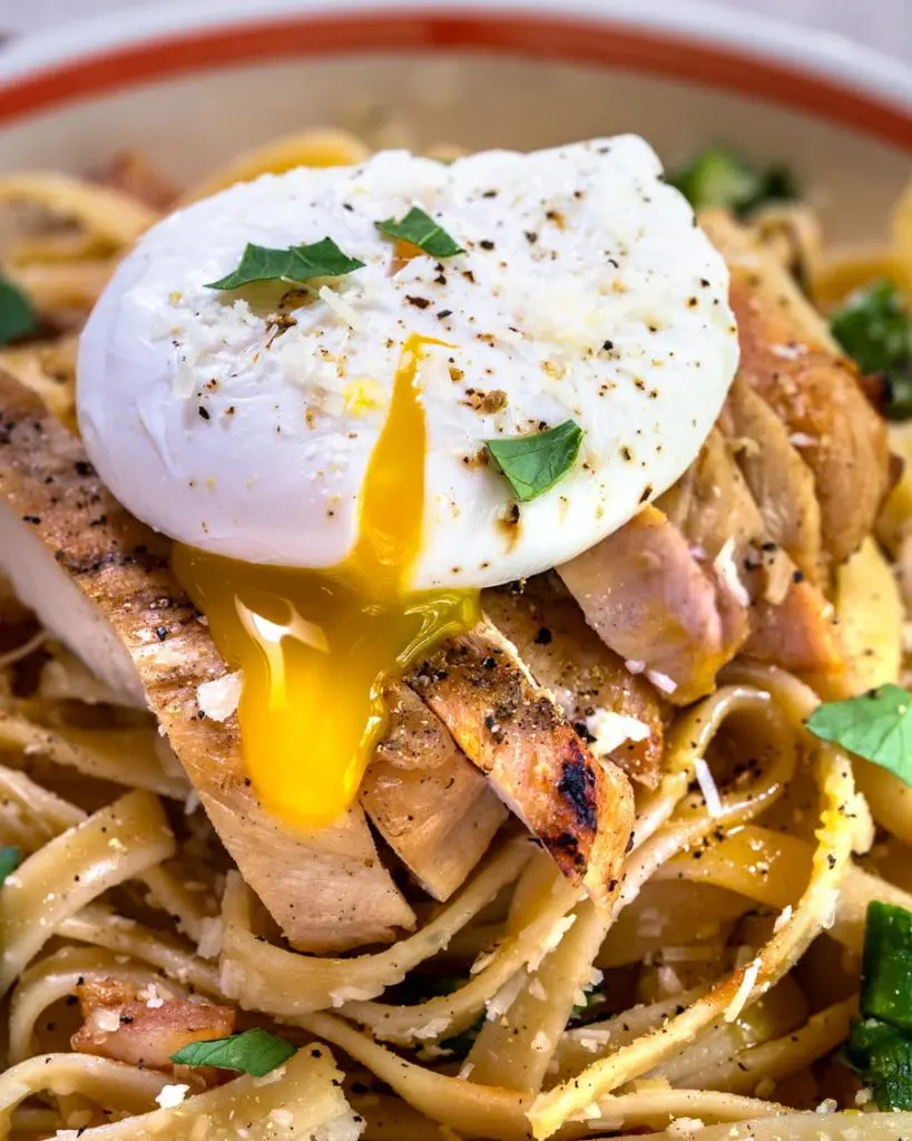 Close up of the yolk of a poached egg running over fettuccine pasta and grilled chicken.