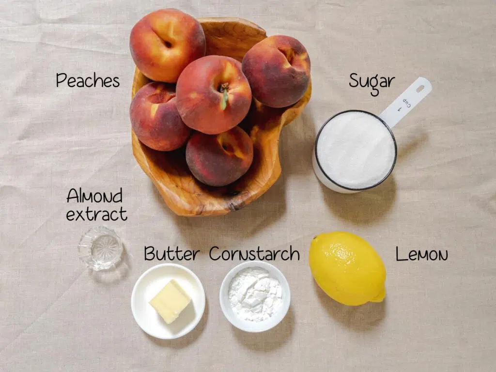 Ingredients used to make peach pie including peaches, almond extract, butter, cornstarch, lemon, and sugar.
