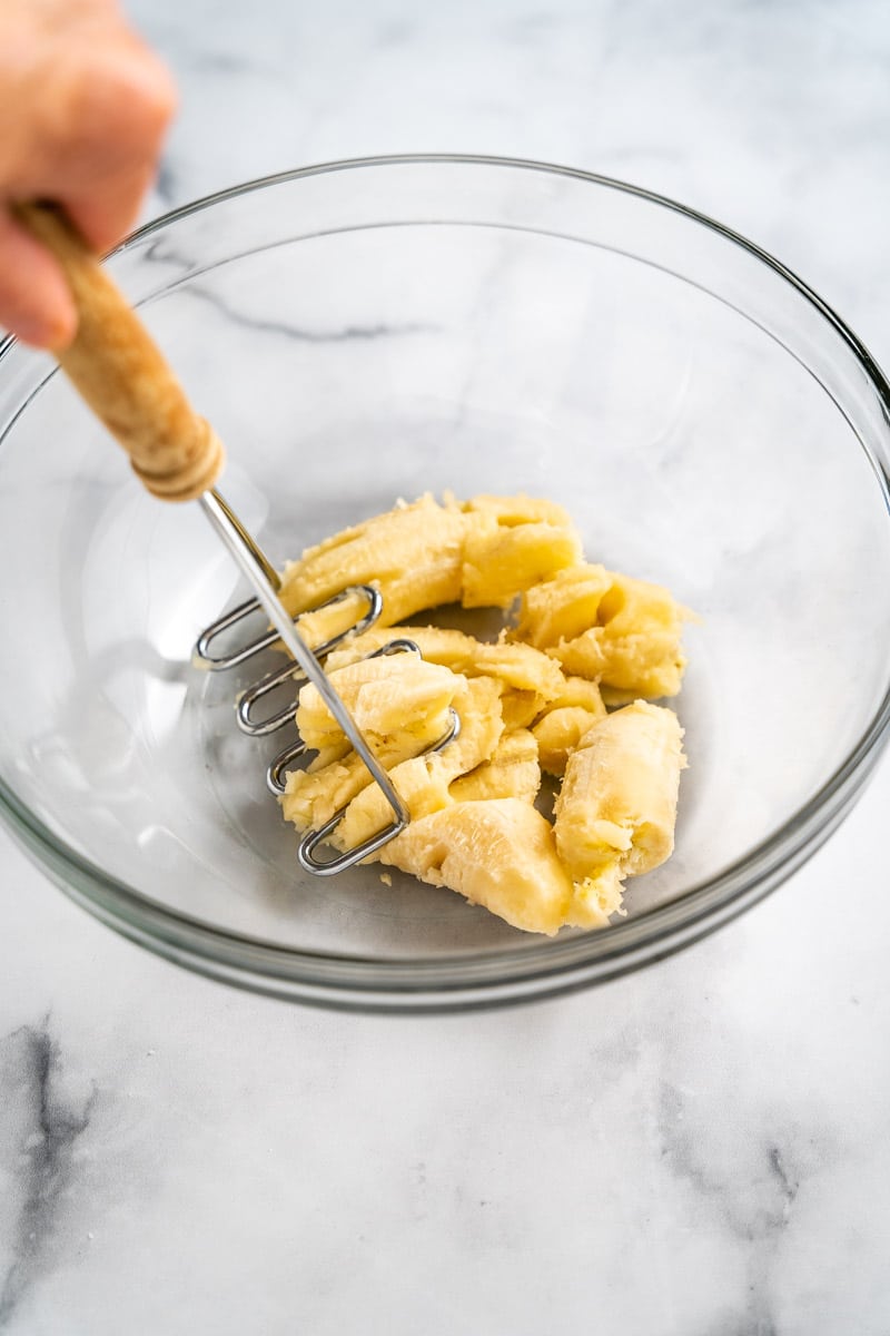 A potato mashed being used to mash bananas in a mixing bowl.