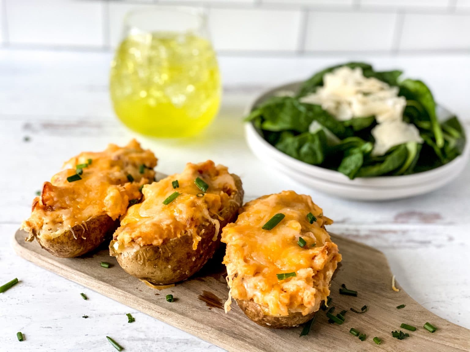 Three twice-baked potatoes in an image with a drink and salad,