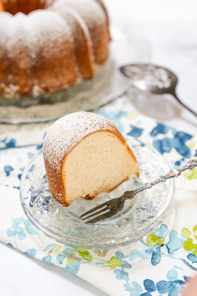 A slice of Kentucky butter cake standing on in on a serving plate. The whole cake sits in the background.