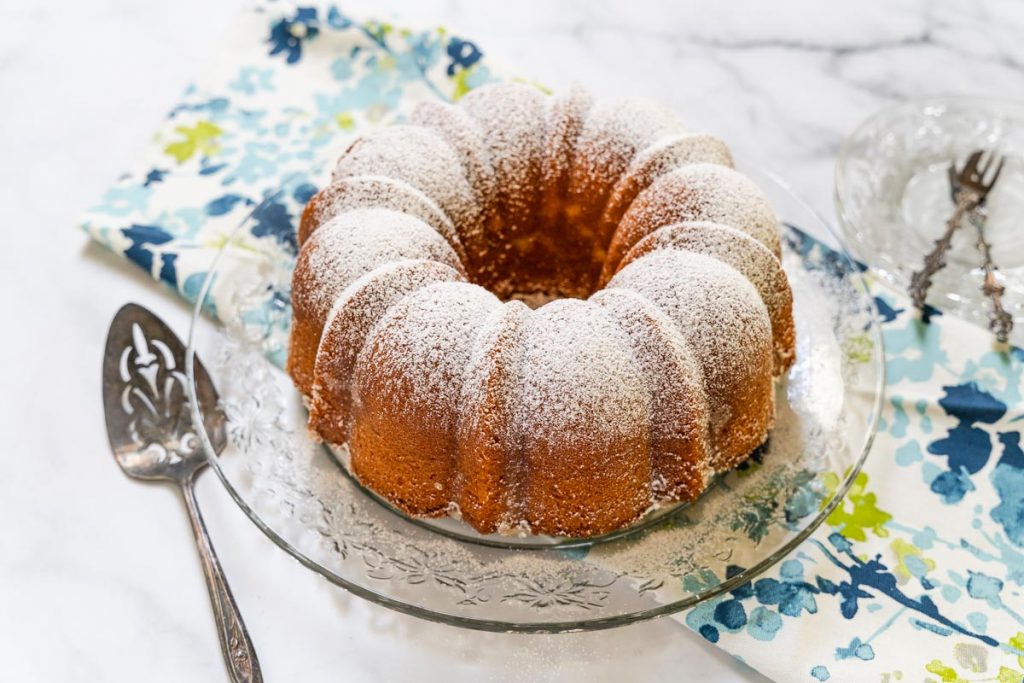 3/4 view of a powder sugar dusted Kentucky Butter cake sitting on a cake plate over a multi-colored napkin.