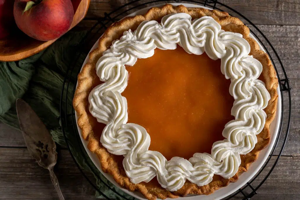 Top down view of a glazed fresh peach pie decorated with a piped whip cream.