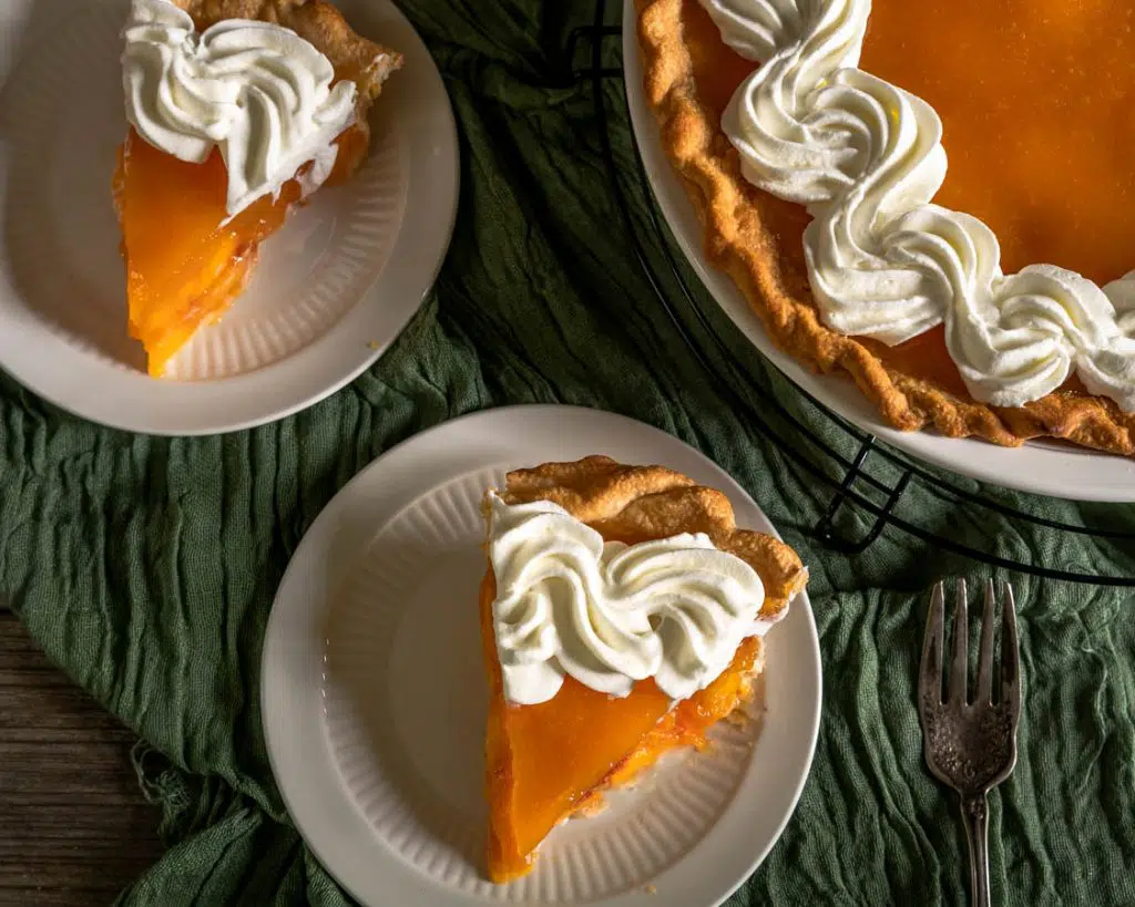 Top down view of two slices of peach pie garnished with whipped cream with a partial view of the whole pie in the background.