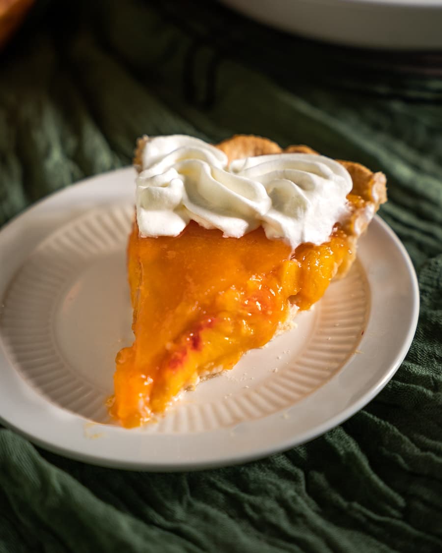 Table view of a slice of fresh peach pie with a whip cream garnish.