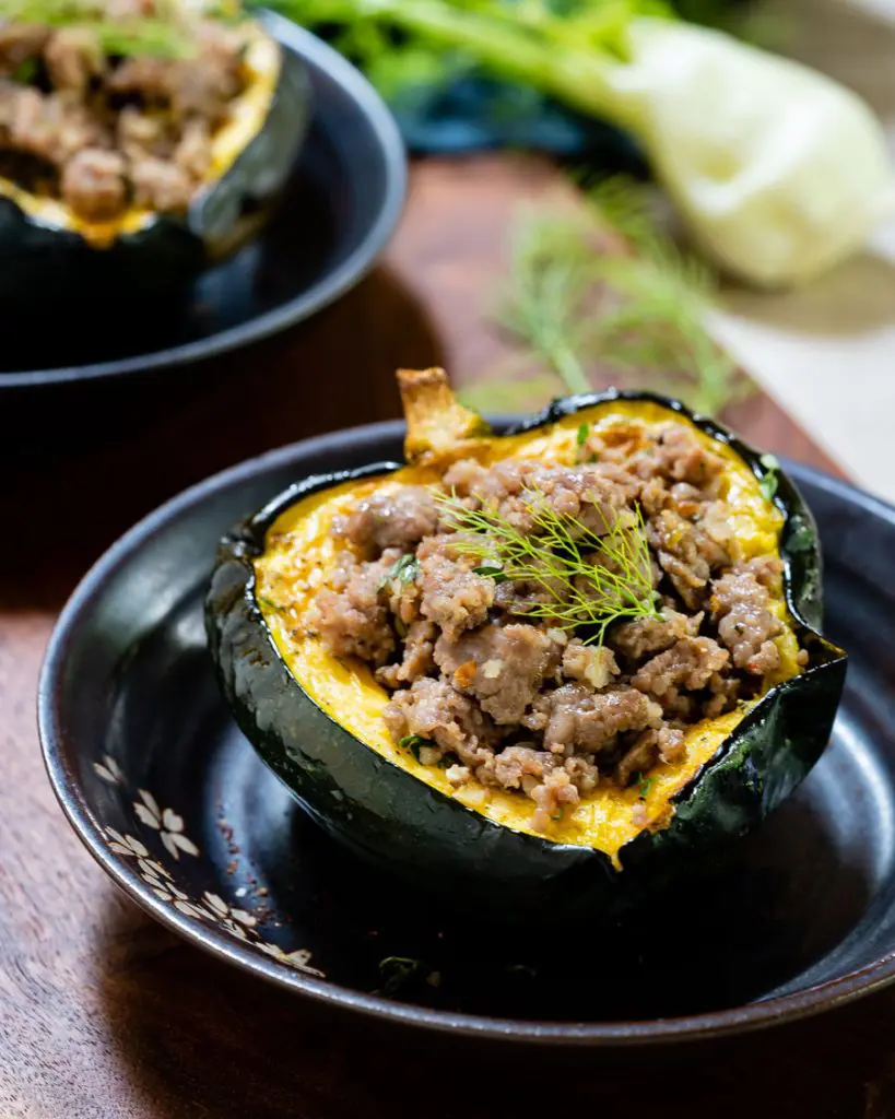 Close-up of sausage-stuffed acorn squash with fennel frond on top.