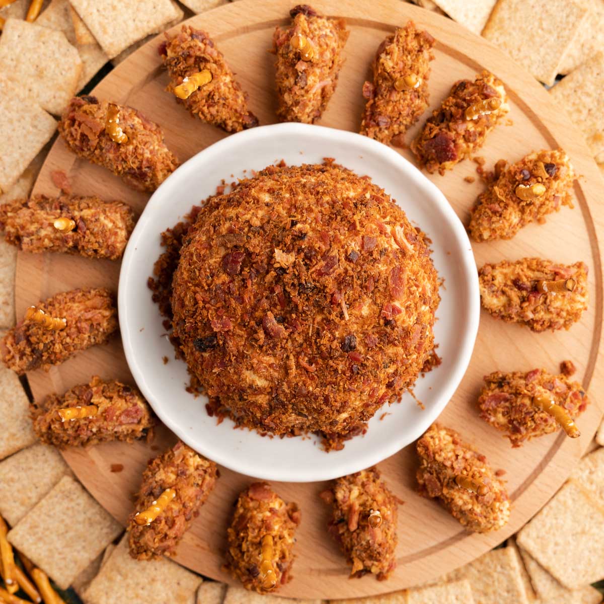 Top down photo of a round bacon covered cheeseball surrounded by football shaped mini cheeseballs