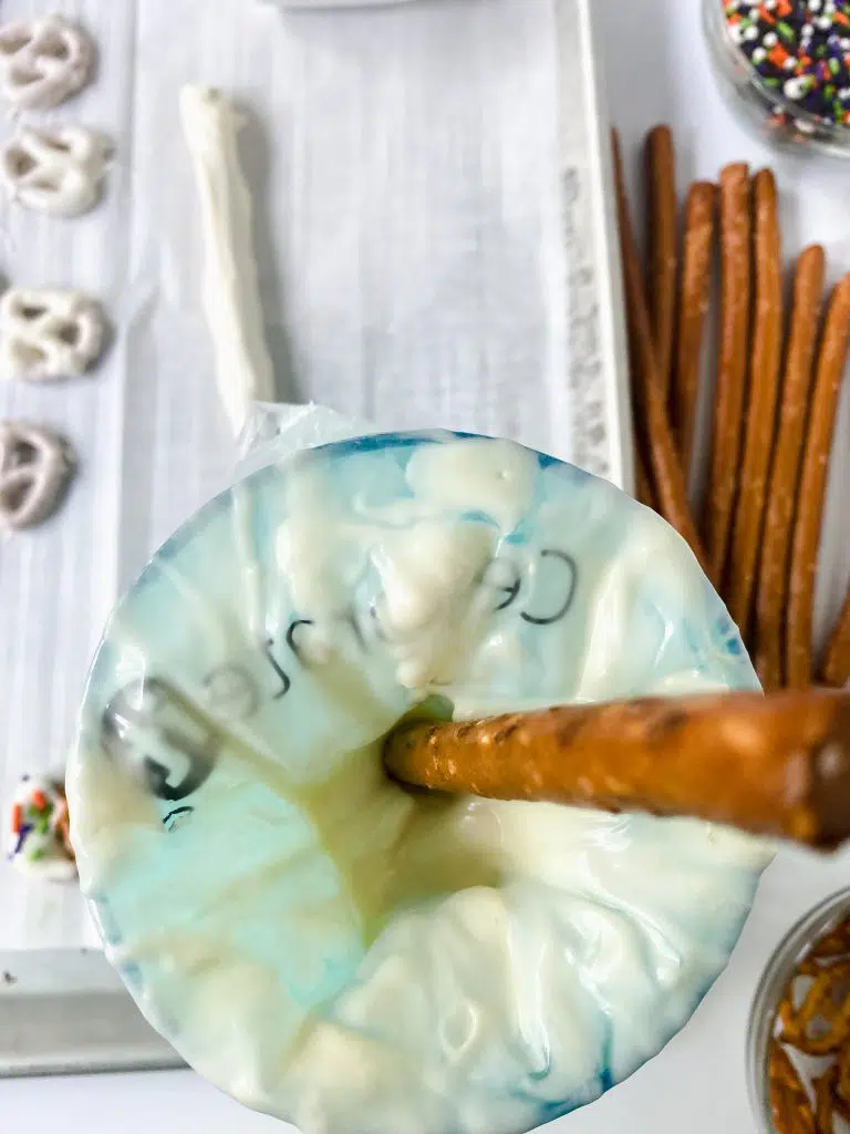 Dipping long pretzel rods in chocolate using a tall cup and piping bag.